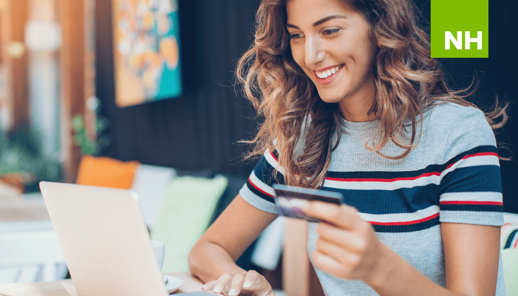 Woman holding credit card while smiling at computer